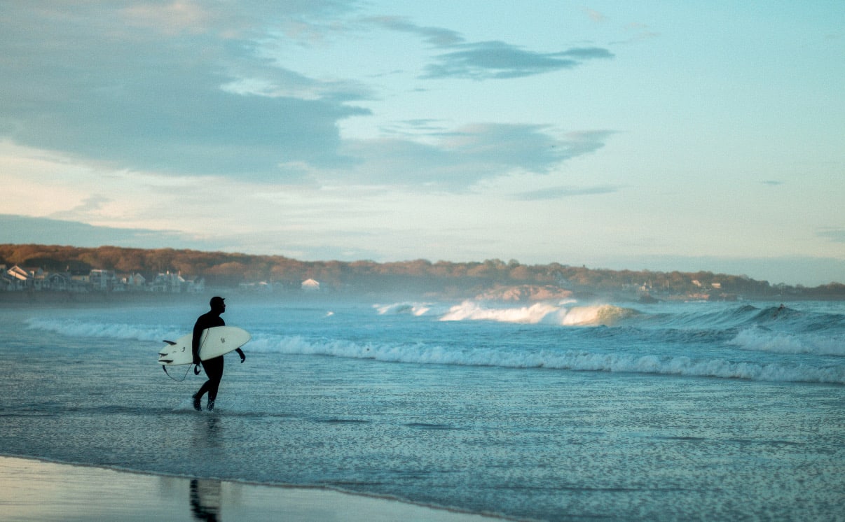 A surfer walking into the ocean at dawn